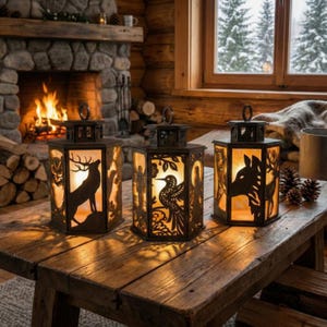 May include: Three decorative metal lanterns with cut-out wildlife silhouettes, including a deer, owl, and bird. The lanterns are lit from within, casting warm light. They sit on a rustic wooden table near a fireplace.