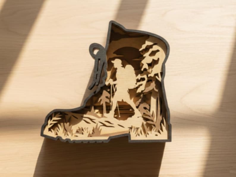 May include: A layered wooden art piece in the shape of a hiking boot. The interior depicts a hiker with a backpack and trekking poles in a forest scene. The boot's outline is dark gray, and the interior layers are light brown.