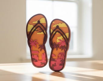 May include: Two wooden flip-flops with a beach scene cut out. The design features a sunset with palm trees, a van, and a dog. The flip-flops are brown with orange, yellow, and pink details, perfect for beach decor.