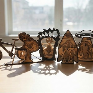 May include: A collection of wooden laser-cut decorative items, including a bicycle, a dinosaur, a bear paw, a mountain scene, and a UFO over a mountain range. The items are brown and sit on a light-colored surface.