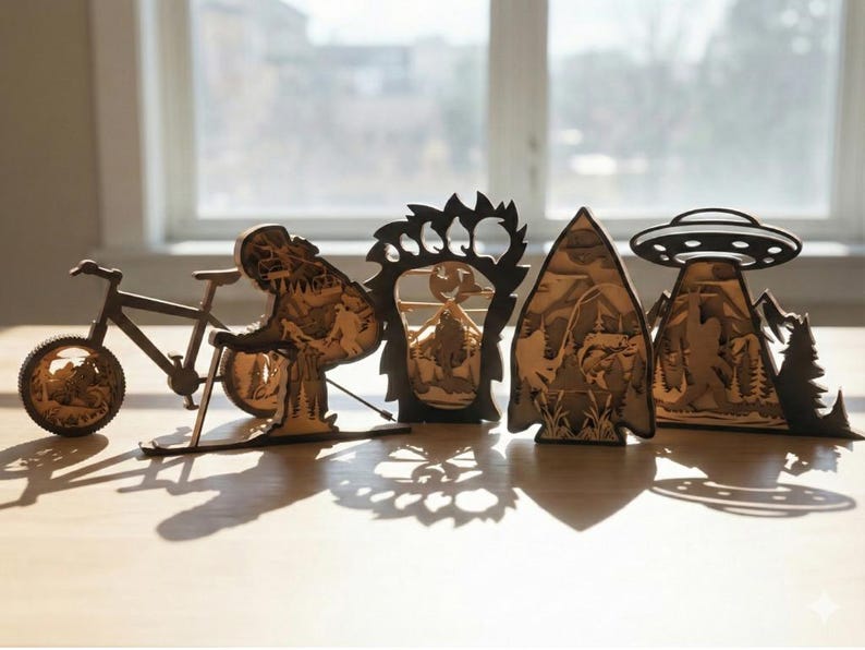 May include: A collection of wooden laser-cut decorative items, including a bicycle, a dinosaur, a bear paw, a mountain scene, and a UFO over a mountain range. The items are brown and sit on a light-colored surface.