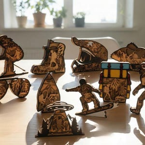 Puede incluir: Colección de figuras de madera cortadas con láser que representan temas de aventura al aire libre. El conjunto incluye un esquiador, un snowboarder, un excursionista, Bigfoot, un pez, una mochila, una bota, un casco y una escena de ovni. Las figuras son de madera marrón claro.