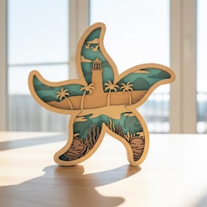 May include: A wooden starfish-shaped art piece with a layered design. The layers depict a coastal scene with a lighthouse, palm trees, and ocean elements in shades of beige, blue, and brown. The artwork is displayed on a light-colored wooden surface.
