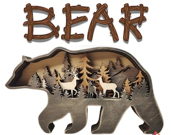May include: A layered wooden bear cutout with a forest scene inside. The bear is brown and the forest scene is made up of trees, deer, and mountains. The word "BEAR" is spelled out in wooden letters above the bear.