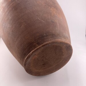 Puede incluir: Un jarr&oacute;n de cer&aacute;mica grande, marr&oacute;n, de estilo antiguo, con cuerpo redondeado y base plana. El jarr&oacute;n tiene una superficie texturizada y un color marr&oacute;n oscuro, con variaciones de tono. El jarr&oacute;n es probablemente hecho a mano y tiene un aspecto r&uacute;stico.