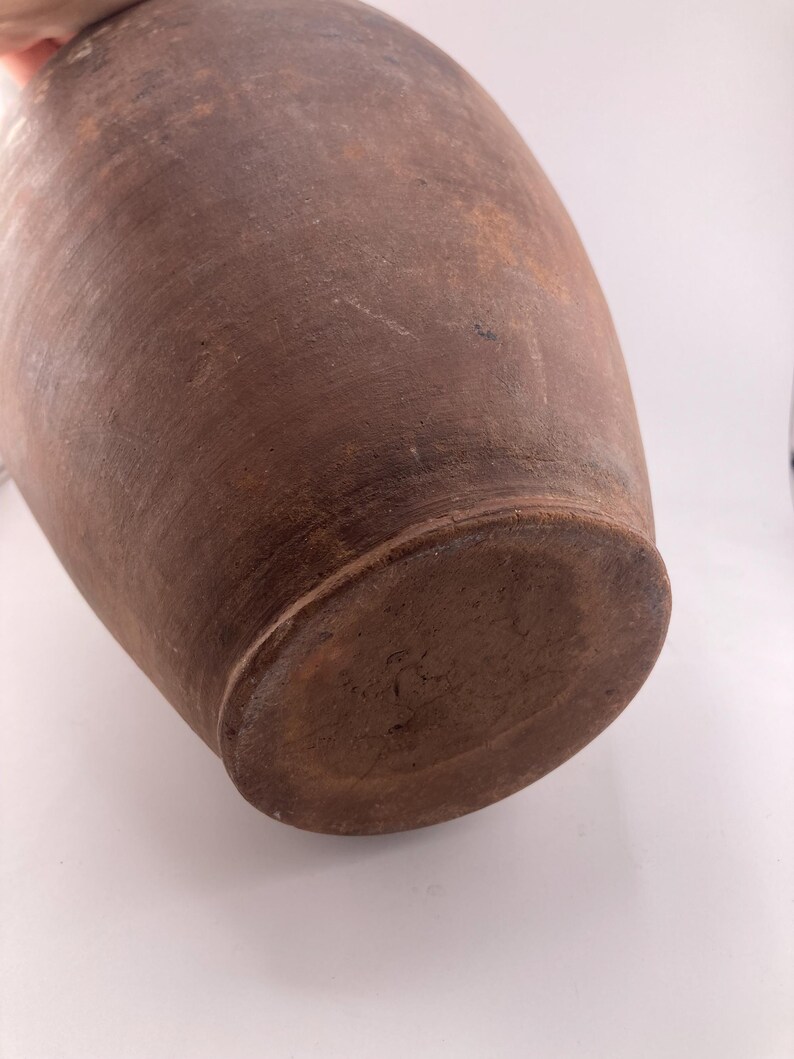 Puede incluir: Un jarr&oacute;n de cer&aacute;mica grande, marr&oacute;n, de estilo antiguo, con cuerpo redondeado y base plana. El jarr&oacute;n tiene una superficie texturizada y un color marr&oacute;n oscuro, con variaciones de tono. El jarr&oacute;n es probablemente hecho a mano y tiene un aspecto r&uacute;stico.