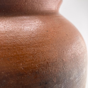 Puede incluir: Primer plano de un jarr&oacute;n de cer&aacute;mica marr&oacute;n con una superficie texturizada. El jarr&oacute;n tiene un cuerpo redondeado y un borde ligeramente ensanchado. El color pasa de un marr&oacute;n m&aacute;s claro en la parte superior a un marr&oacute;n m&aacute;s oscuro en la inferior.