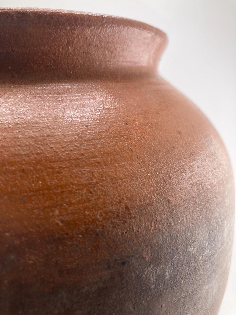 Puede incluir: Primer plano de un jarr&oacute;n de cer&aacute;mica marr&oacute;n con una superficie texturizada. El jarr&oacute;n tiene un cuerpo redondeado y un borde ligeramente ensanchado. El color pasa de un marr&oacute;n m&aacute;s claro en la parte superior a un marr&oacute;n m&aacute;s oscuro en la inferior.