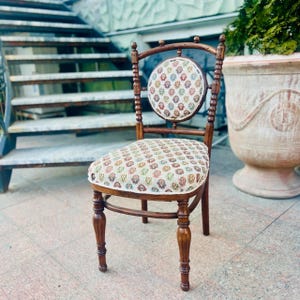 May include: A vintage wooden chair with a round back and seat. The chair has a dark brown finish with ornate detailing. The seat and back are upholstered with a patterned fabric in shades of red, green, and yellow.