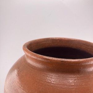 Puede incluir: Un jarr&oacute;n de cer&aacute;mica marr&oacute;n con una abertura ancha y un cuerpo redondeado. El jarr&oacute;n tiene un acabado liso y brillante y una superficie ligeramente texturizada. El color es un marr&oacute;n c&aacute;lido y terroso, lo que sugiere una est&eacute;tica r&uacute;stica o vintage.