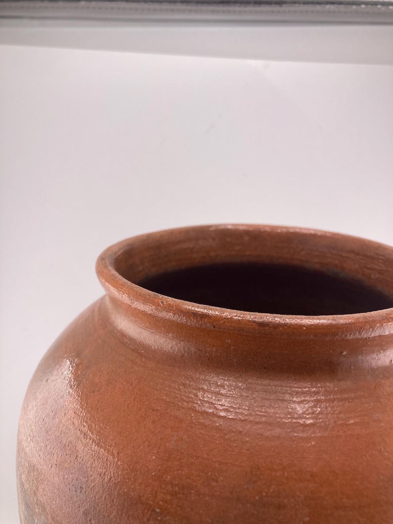 Puede incluir: Un jarr&oacute;n de cer&aacute;mica marr&oacute;n con una abertura ancha y un cuerpo redondeado. El jarr&oacute;n tiene un acabado liso y brillante y una superficie ligeramente texturizada. El color es un marr&oacute;n c&aacute;lido y terroso, lo que sugiere una est&eacute;tica r&uacute;stica o vintage.