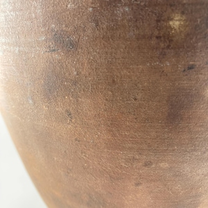 Puede incluir: Primer plano de un recipiente de cer&aacute;mica marr&oacute;n texturizado. La superficie tiene un aspecto moteado con variaciones de color, que van del beige claro al marr&oacute;n oscuro. La forma del recipiente es parcialmente visible, sugiriendo una forma redondeada.