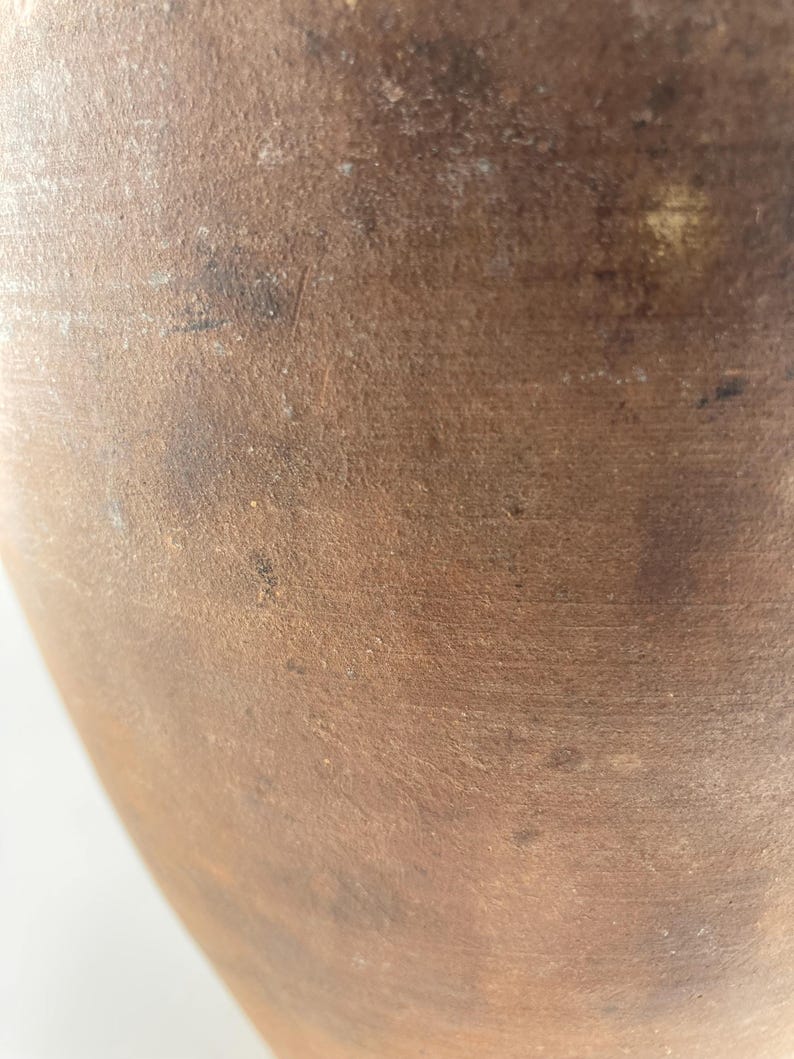 Puede incluir: Primer plano de un recipiente de cer&aacute;mica marr&oacute;n texturizado. La superficie tiene un aspecto moteado con variaciones de color, que van del beige claro al marr&oacute;n oscuro. La forma del recipiente es parcialmente visible, sugiriendo una forma redondeada.