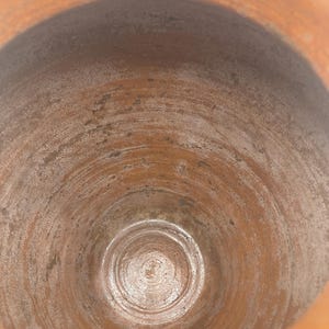 Puede incluir: Vista de cerca del interior de una olla de cer&aacute;mica de color terracota. El interior muestra patrones circulares conc&eacute;ntricos y una superficie texturizada. El borde de la olla es visible en la parte superior, con un tono ligeramente m&aacute;s claro del mismo color.