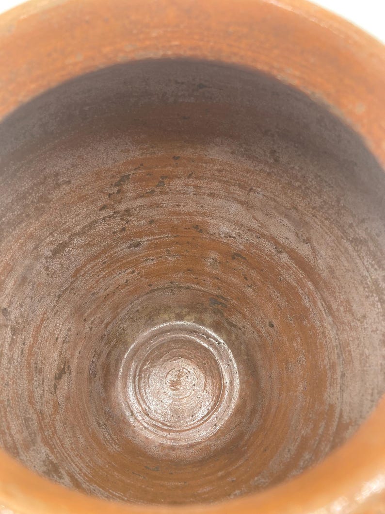 Puede incluir: Vista de cerca del interior de una olla de cer&aacute;mica de color terracota. El interior muestra patrones circulares conc&eacute;ntricos y una superficie texturizada. El borde de la olla es visible en la parte superior, con un tono ligeramente m&aacute;s claro del mismo color.