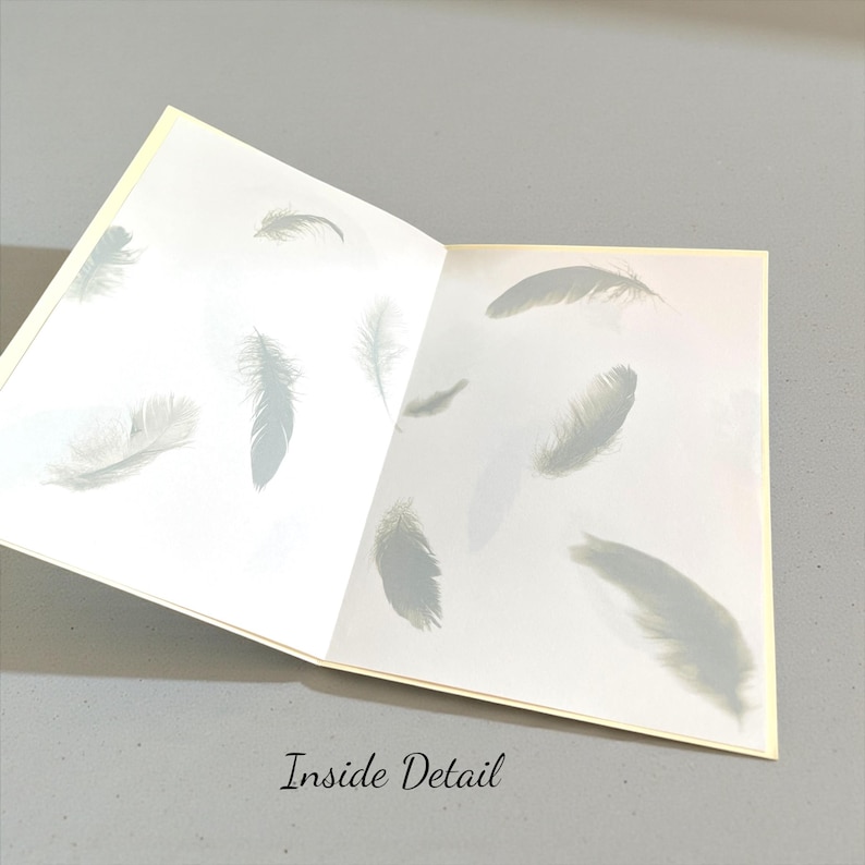 May include: Open greeting card with a soft yellow border, revealing a white interior adorned with delicate gray feather illustrations. The text "Inside Detail" is printed at the bottom of the card.