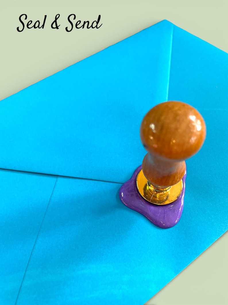 May include: A wooden handled wax seal stamp with a gold base, pressing into a purple wax seal on a bright blue envelope. The words "Seal & Send" are in the upper left corner.