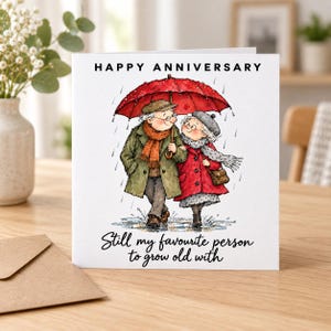 May include: A square greeting card featuring a watercolour illustration of an elderly couple walking under a red umbrella in the rain. The text reads HAPPY ANNIVERSARY and Still my favourite person to grow old with in black lettering.