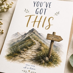Può includere: Un biglietto d'auguri con un'illustrazione ad acquerello di un sentiero in pietra che sale su una montagna. Il testo recita YOU'VE GOT THIS in blu scuro e oro, con un cartello in legno KEEP GOING e la frase One step at a time sotto.