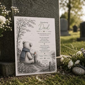 Op de afbeelding: Een herdenkingskaart met de tekst "Remembering Dad" toont een teddybeer met een blauwe sjaal, zittend bij een boom. De kaart bevat een gedicht en is geplaatst in de buurt van een grafsteen, met bloemen op de voorgrond.