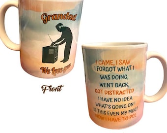 May include: A white ceramic mug with a handle, featuring a design with the word "Grandad" and a silhouette of a person. The back of the mug has humorous text. The mug has a colorful, watercolor-style background.