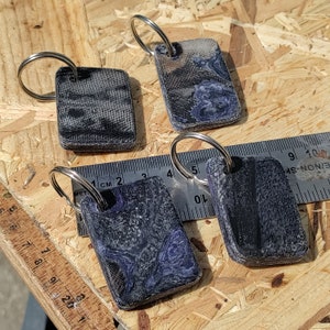 Puede incluir: Cuatro llaveros con diferentes diseños. Cada llavero presenta un patrón de mármol negro y azul. Los llaveros están hechos de un material duradero y tienen un anillo de metal plateado.
