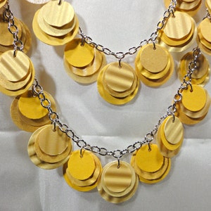 May include: A gold necklace with a chain and multiple layers of round, overlapping, gold-toned discs.