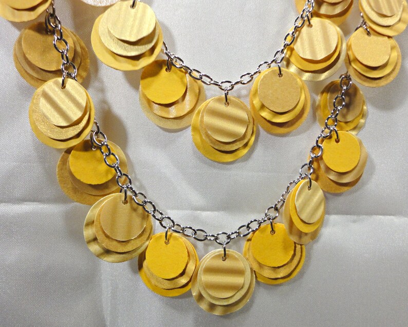 May include: A gold necklace with a chain and multiple layers of round, overlapping, gold-toned discs.