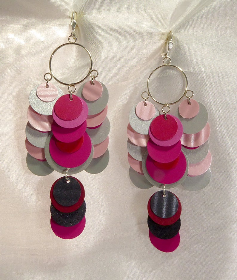 May include: A pair of dangle earrings with multiple layers of pink, silver, and black circles. The earrings are made of felt and have a silver hook closure.