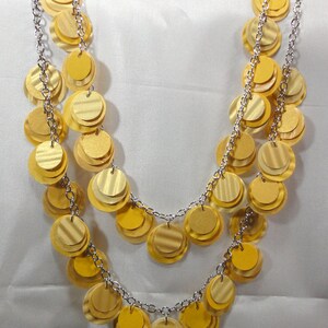 May include: A gold necklace with multiple layers of round, overlapping, metallic discs. The necklace is made of silver chain.