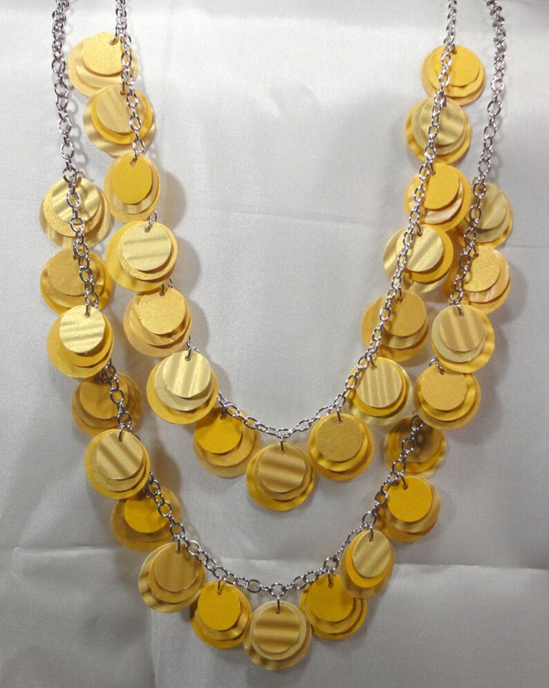 May include: A gold necklace with multiple layers of round, overlapping, metallic discs. The necklace is made of silver chain.