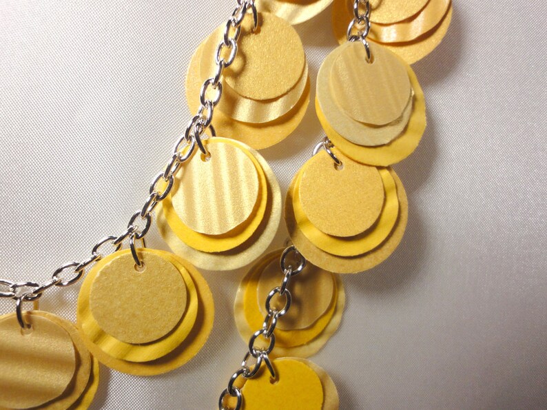 May include: A silver chain necklace with multiple layers of yellow paper circles. The circles are layered on top of each other to create a cascading effect.
