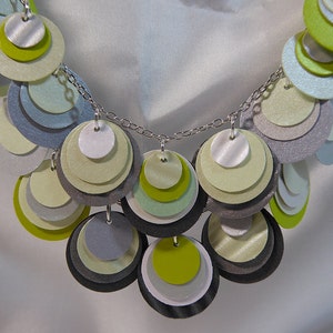 May include: A silver chain necklace with layered circles of green, gray, and white paper. The circles are arranged in a cascading pattern.