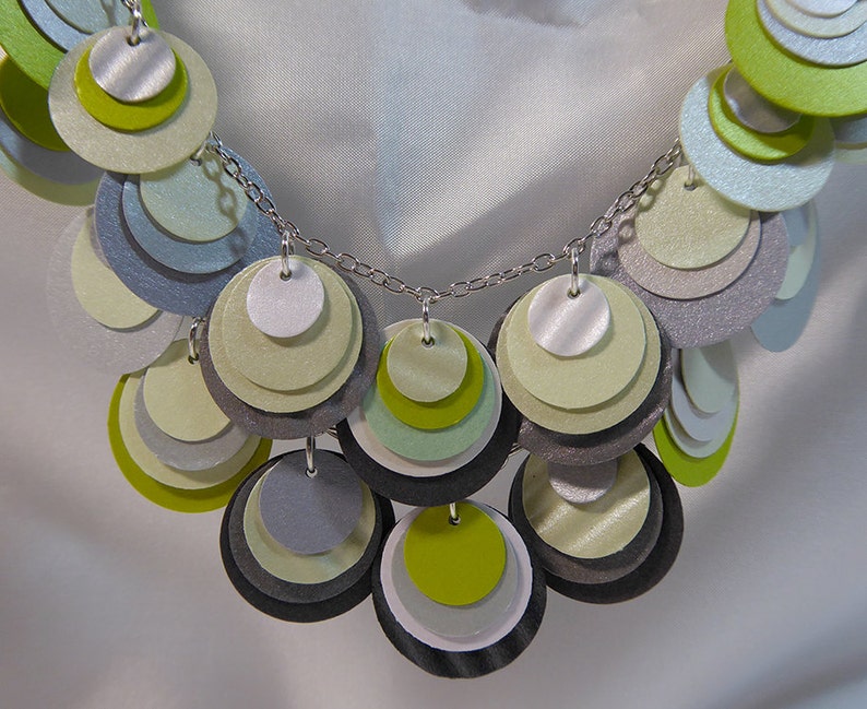 May include: A silver chain necklace with layered circles of green, gray, and white paper. The circles are arranged in a cascading pattern.
