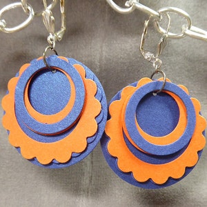 May include: A pair of clip-on earrings with three layers of circles. The outer layer is orange with scalloped edges, the middle layer is blue, and the inner layer is a smaller blue circle.