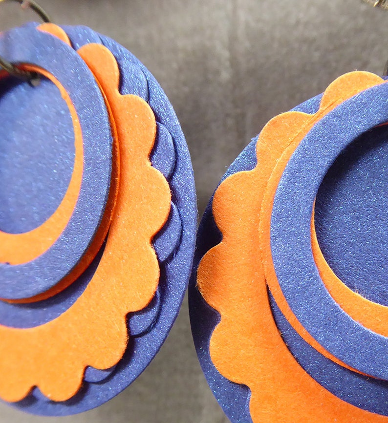 May include: A pair of earrings made of layered felt circles. The circles are orange and blue, with the blue circles having a scalloped edge.