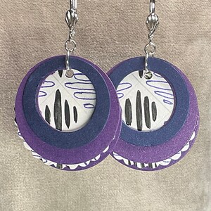 May include: Purple and white layered circle earrings with a black and white abstract design. The earrings have silver hooks.
