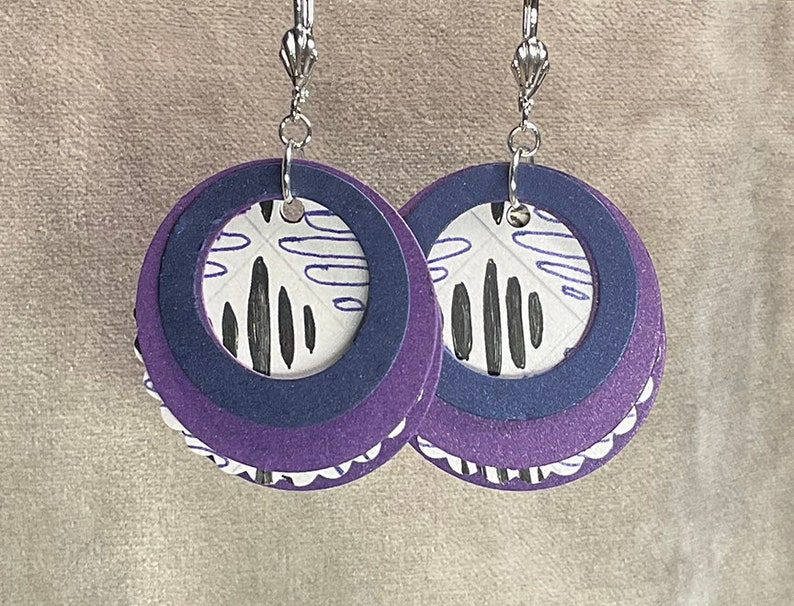 May include: Purple and white layered circle earrings with a black and white abstract design. The earrings have silver hooks.