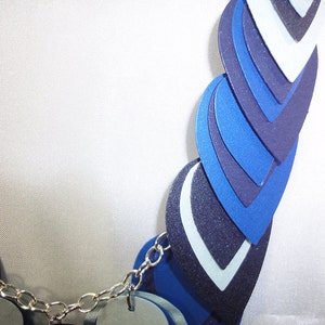May include: A blue and white layered necklace with a silver chain. The necklace is made of multiple layers of blue and white fabric, each layer is a different shade of blue. The necklace is a statement piece and would be perfect for a special occasion.