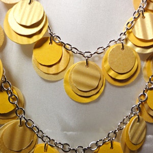 May include: A silver chain necklace with multiple layers of yellow paper circles. The circles are layered on top of each other to create a cascading effect.