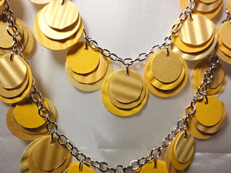 May include: A silver chain necklace with multiple layers of yellow paper circles. The circles are layered on top of each other to create a cascading effect.