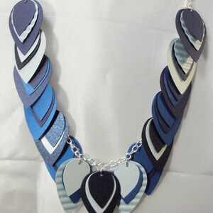 May include: A necklace made of layered blue, white, and black paper teardrop shapes. The necklace is strung on a silver chain.