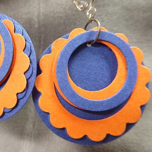 May include: A pair of earrings with a layered design. The earrings are made of orange and blue felt and have a scalloped edge. The earrings are attached to silver hooks.