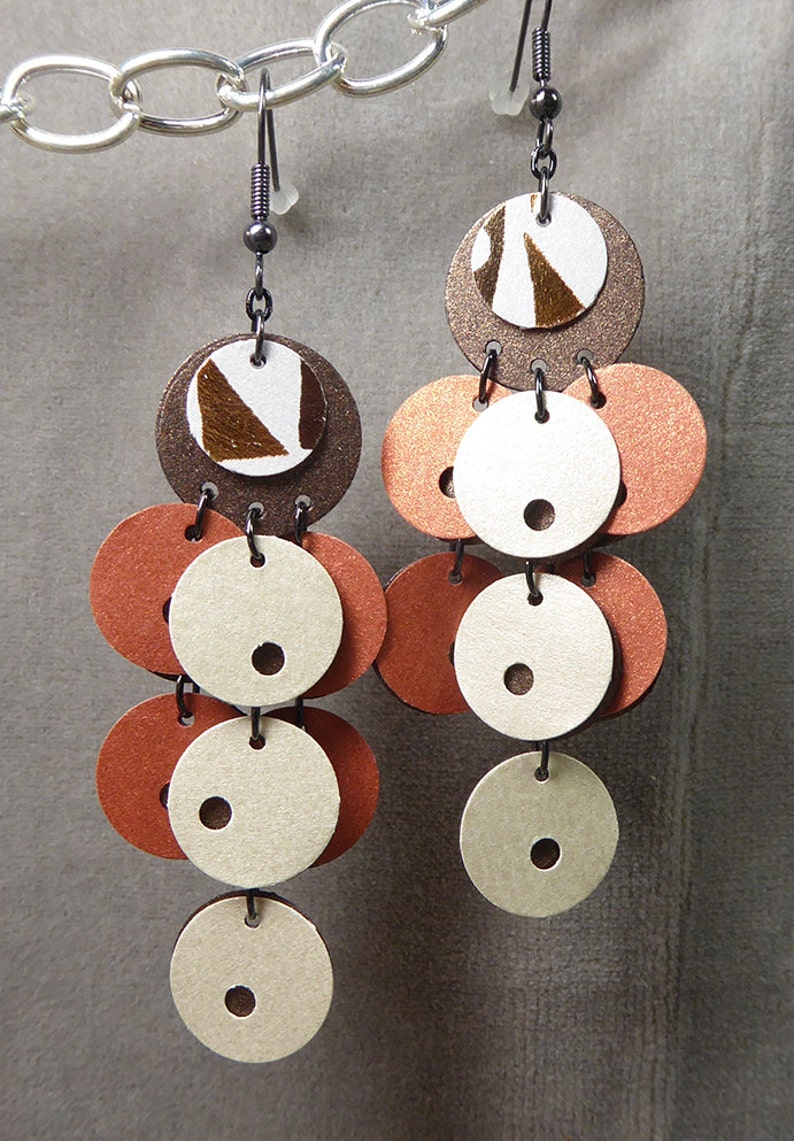 May include: A pair of dangle earrings with multiple layers of brown, white, and orange circles. The circles are made of leather and have a textured finish.