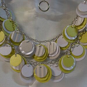 May include: A silver chain necklace with multiple layers of round, layered paper circles in shades of white, yellow, and green.