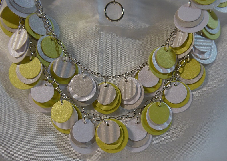 May include: A silver chain necklace with multiple layers of round, layered paper circles in shades of white, yellow, and green.