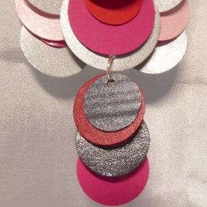 May include: Silver, pink, and red layered circle earrings with a sparkly silver and red dangle.