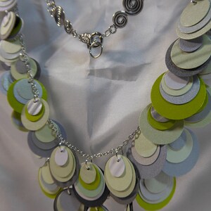 May include: A silver chain necklace with a silver clasp and a layered circle pendant made of green, white, and gray paper.