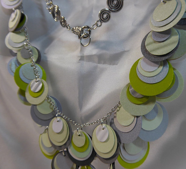 May include: A silver chain necklace with a silver clasp and a layered circle pendant made of green, white, and gray paper.