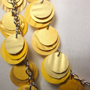 May include: A gold necklace with multiple layers of round, overlapping discs connected by a silver chain.